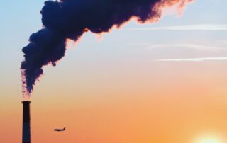 Silhouette of smokestack in front of orange NYC sunset with an airplane in the foreground.