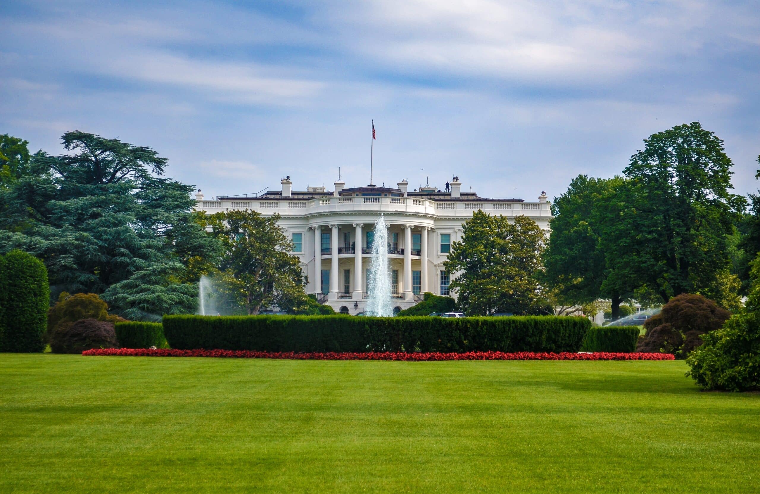 Rear view of the White House with lawn and garden in the foreground and blue sky in the background.