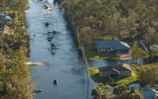 Hurricahe fainfall flooded Florida road with evacuating cars and surrounded with water houses in suburban residential area.