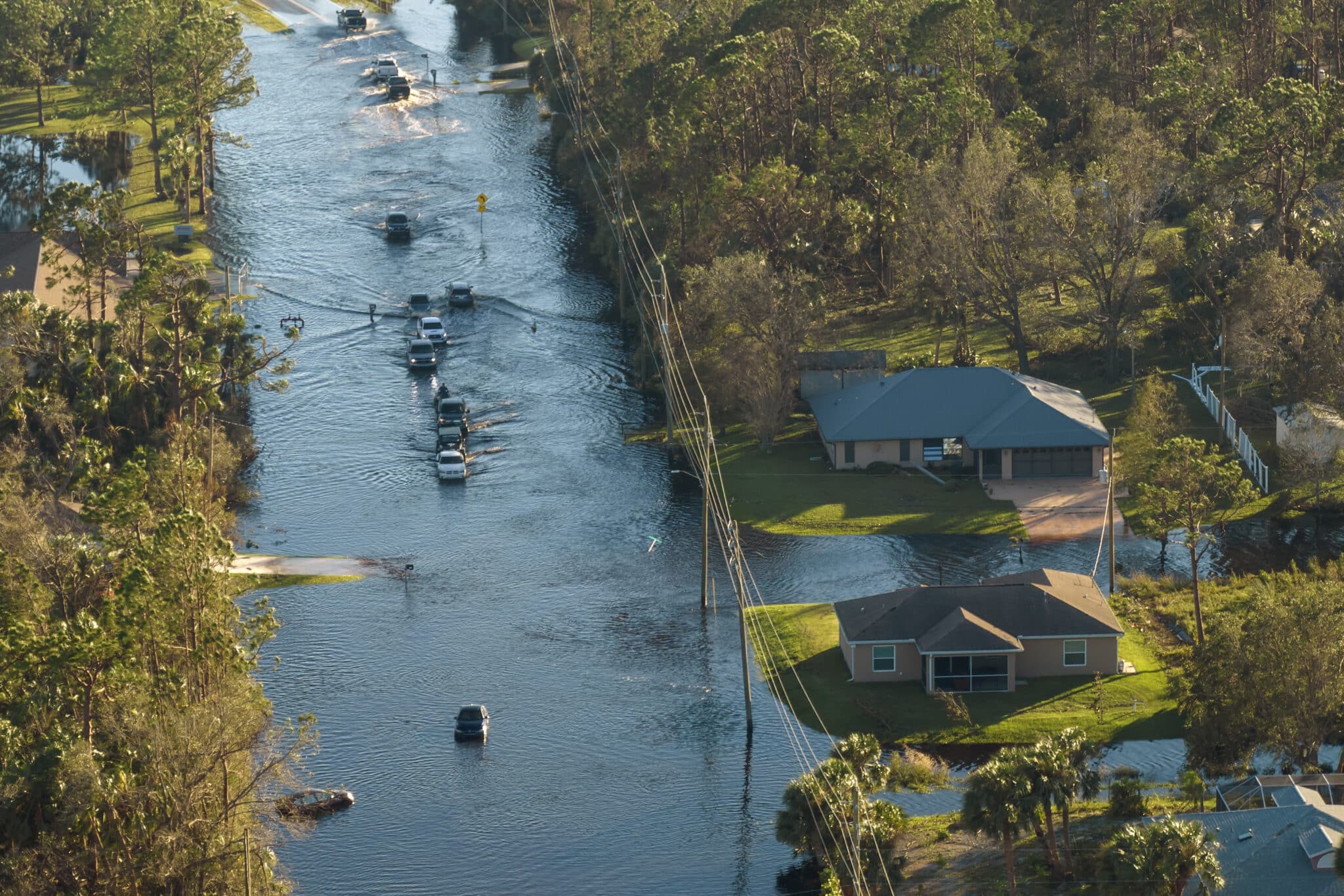 Hurricahe fainfall flooded Florida road with evacuating cars and surrounded with water houses in suburban residential area.