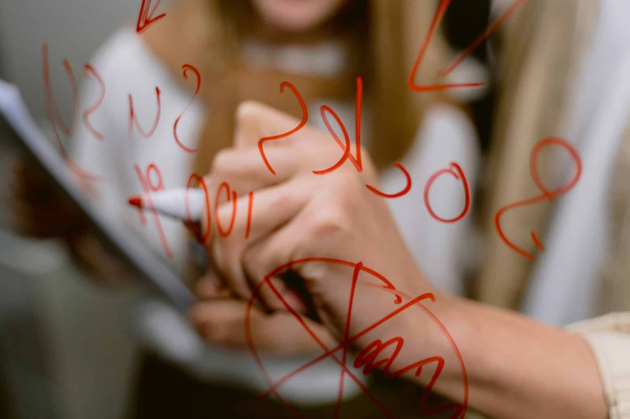Woman with red marker writes calculations on glass surface
