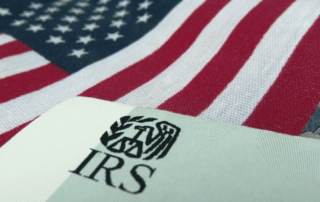 Piece of green paper with the IRS logo on it and a US flag in the background