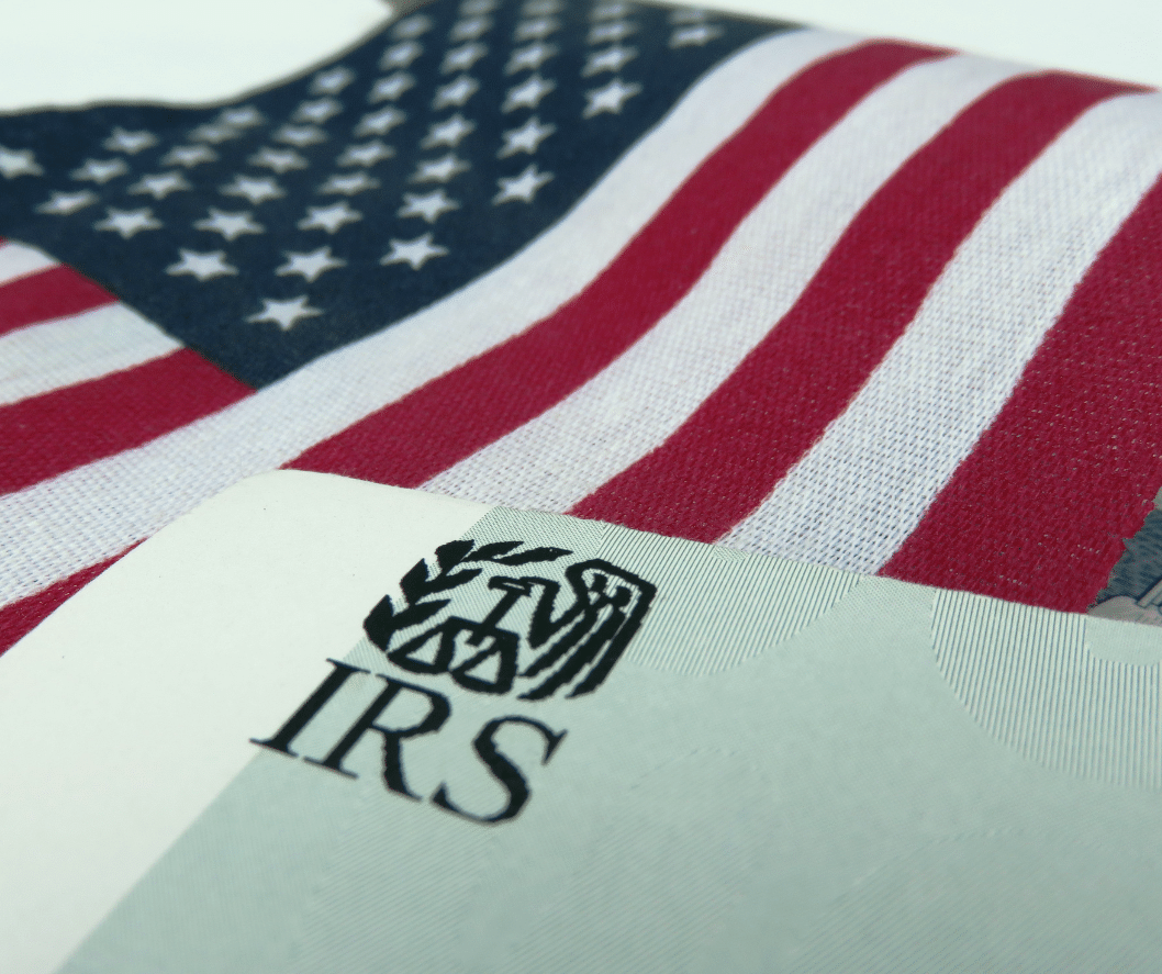 Piece of green paper with the IRS logo on it and a US flag in the background