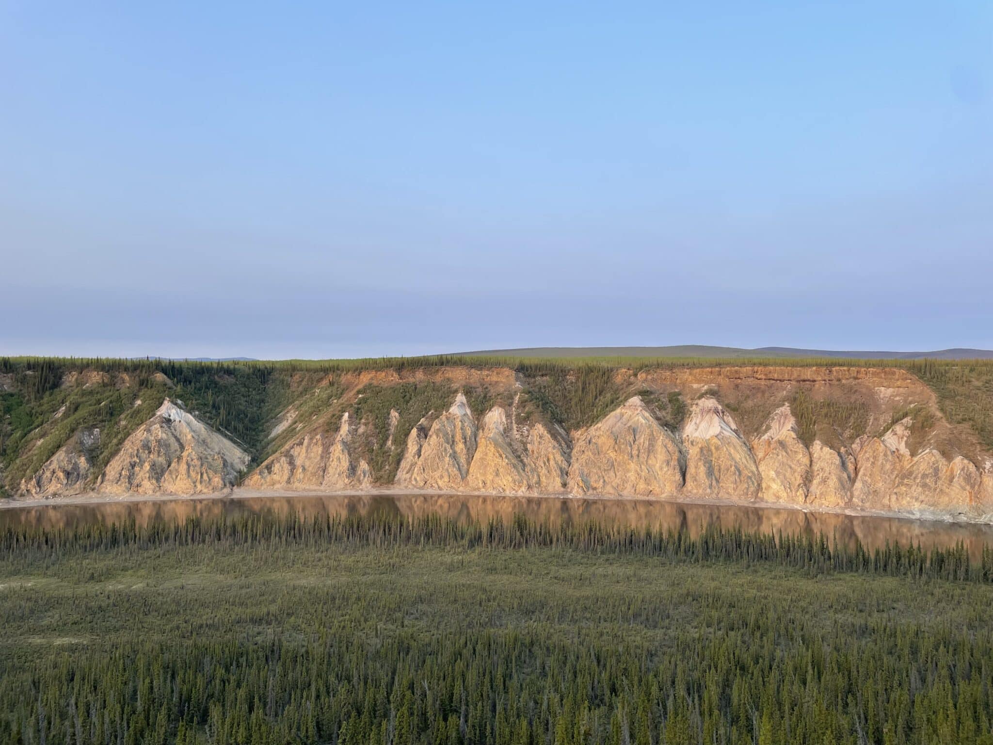 Slate brown bluffs overlooking the Porcupine River with large green pines in the foreground